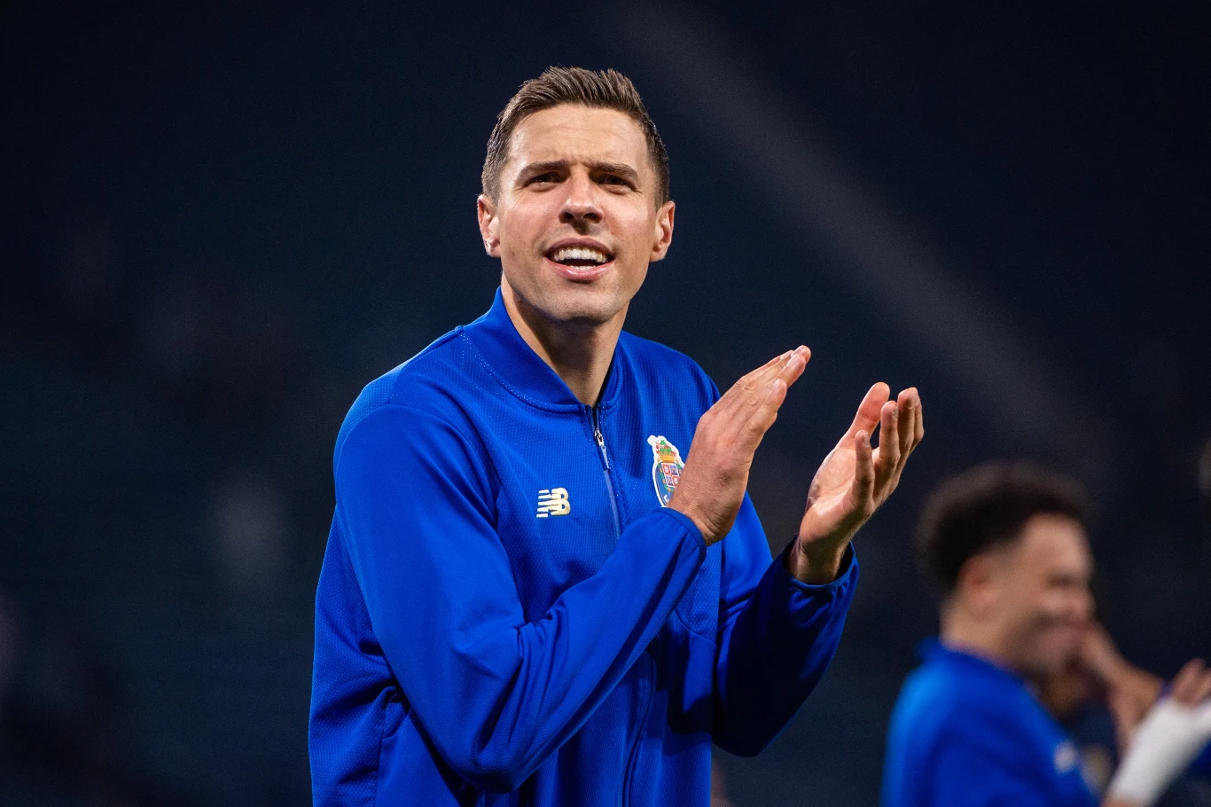 Jan Bednarek Mężczyzna w niebieskim sportowym stroju klaszcze, stojąc na stadionie, z wyraźnym wyrazem radości na twarzy.