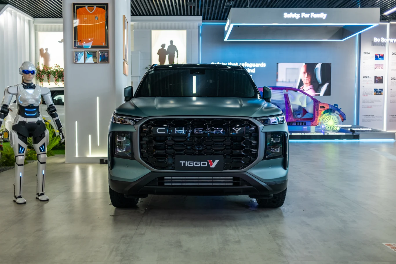Nowoczesny samochód SUV marki Chery Tiggo 7 zaprezentowany na wystawie, obok zaawansowany robot humanoidalny, w tle podświetlone panele z informacjami motoryzacyjnymi.