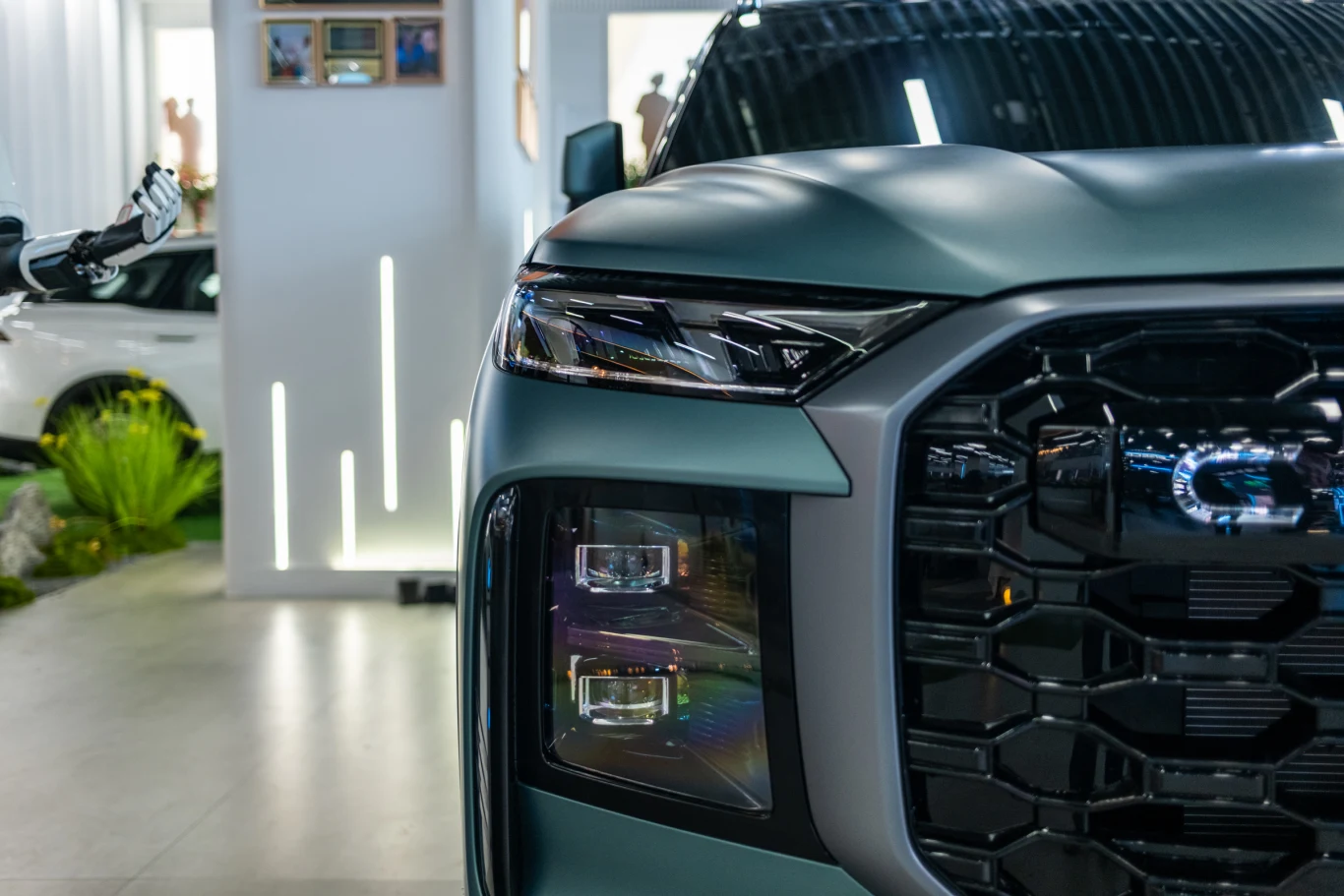 Front nowoczesnego SUV-a z charakterystycznym, masywnym grillem i zintegrowanymi reflektorami LED, ustawionego w jasnym, zamkniętym pomieszczeniu.