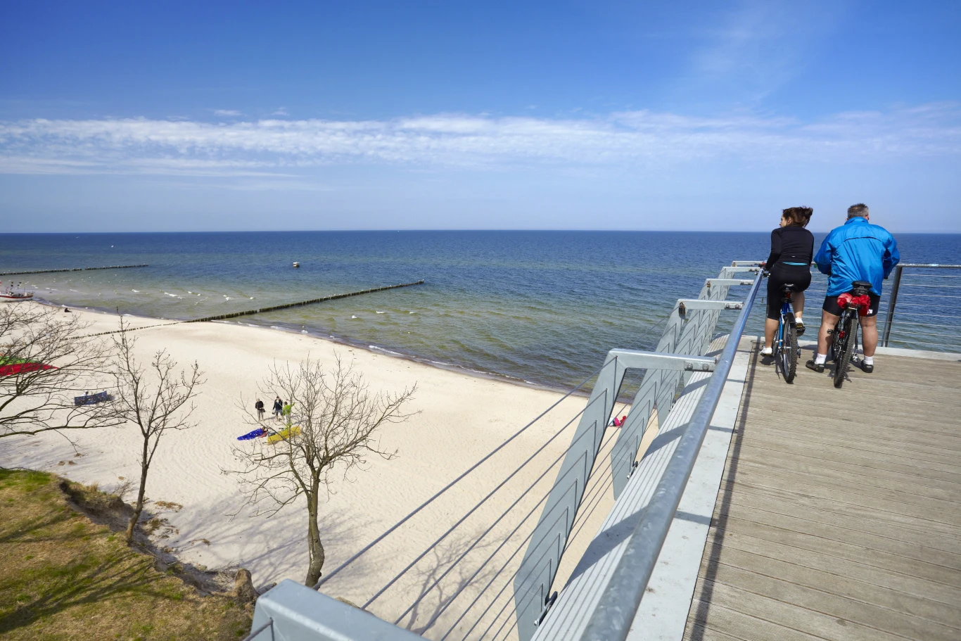Trzęsacz to świetny kierunek dla osób poszukujących spokoju nad Bałtykiem Dwie osoby na rowerach na tarasie widokowym w Trzęsaczu, z widokiem na plażę i Bałtyk.