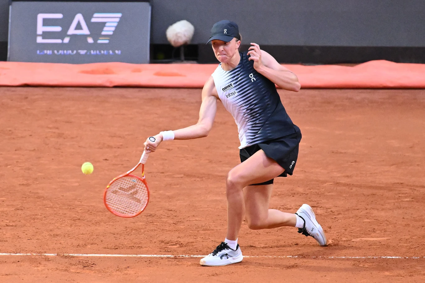 Zawodniczka w sportowym stroju odbija piłkę tenisową rakietą na korcie ziemnym podczas meczu.