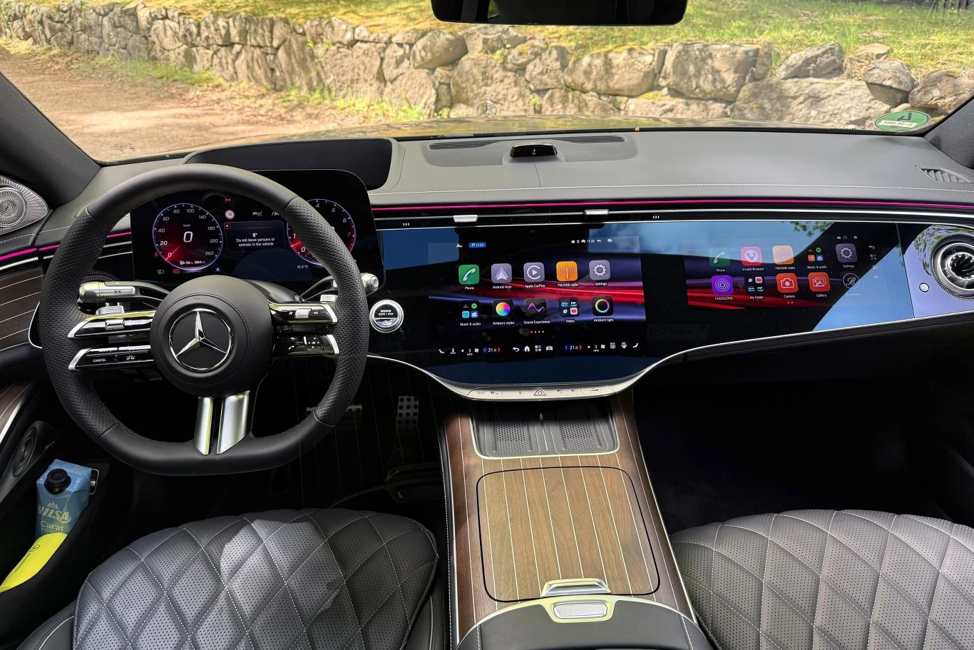 Luksusowe wnętrze samochodu Mercedes z panoramicznym cyfrowym kokpitem i dużym dotykowym wyświetlaczem, skórzane siedzenia z pikowanym wzorem oraz eleganckie drewniane wykończenia konsoli środkowej.