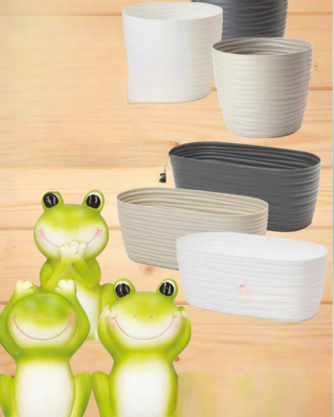 Cztery ceramiczne doniczki w odcieniach bieli, szarości i beżu ustawione w dwóch rzędach, obok trzech dużych figurek uśmiechniętych żab w jaskrawozielonym kolorze.
