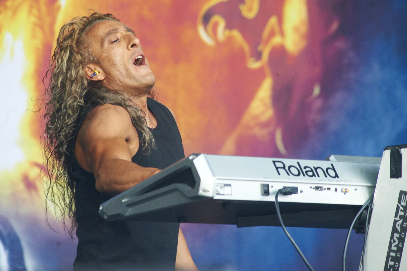 Alex Staropoli stoi na czele grupy Rhapsody of Fire Alex Staropoli z Rhapsody of Fire gra na klawiszach syntezatora Roland, w tle kolorowe światła sceniczne.