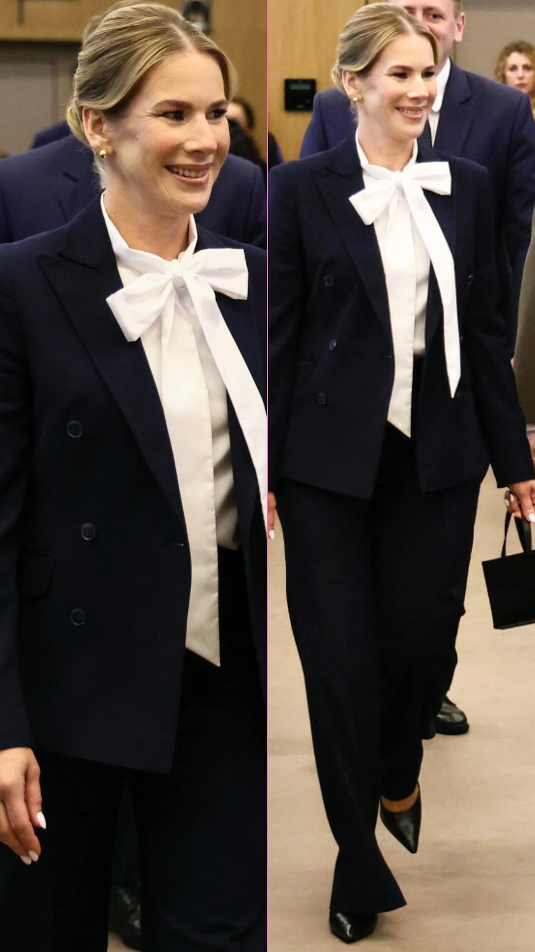 Elegancka kobieta w granatowym garniturze, białej koszuli z dużą kokardą pod szyją i czarnych lakierowanych butach, trzymająca niewielką czarną torebkę.