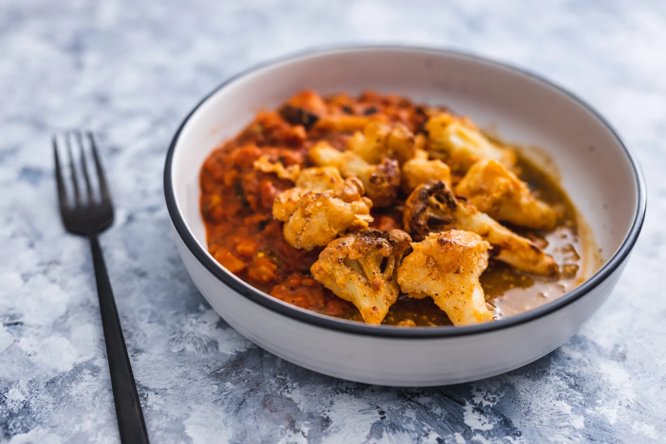 Kalafior w sosie pomidorowym to świetna propozycja na lekki obiad Porcja pieczonego kalafiora w sosie pomidorowym z zielonym pesto, podana w głębokim talerzu.