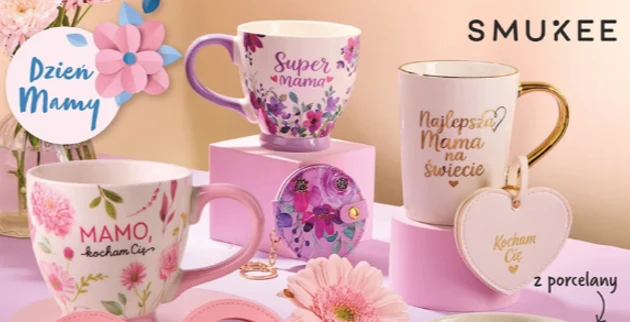 Trzy porcelanowe kubki ozdobione pastelowymi kwiatami i napisami dedykowanymi mamom, ustawione na różowych podstawkach, obok porcelanowe serce z napisem „Kocham Cię” oraz dekoracyjne kwiaty.