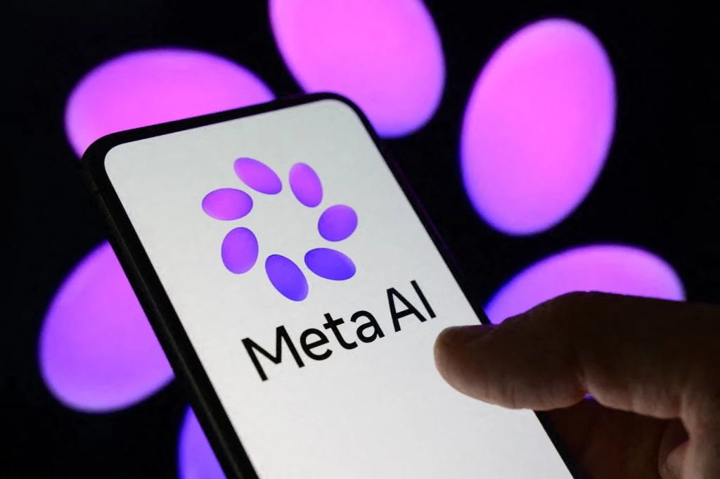Logo Meta AI wyświetlone na ekranie smartfona, trzymanym przez dłoń, na tle rozmytych, fioletowych świateł.