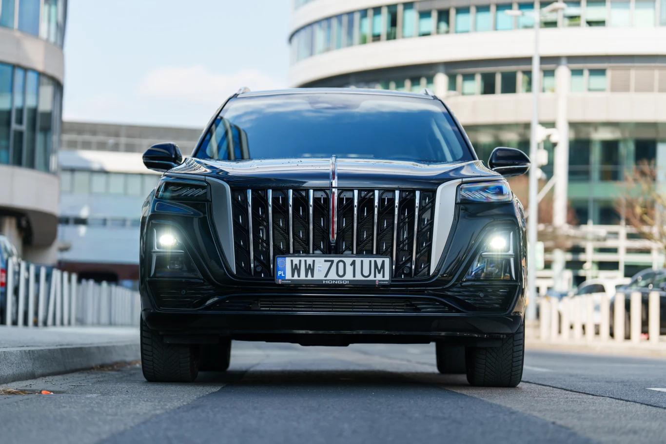 Czarny luksusowy SUV z charakterystycznym, pionowym grillem oraz nowoczesnymi światłami LED zaparkowany na ulicy w centrum miasta otoczonym biurowcami.