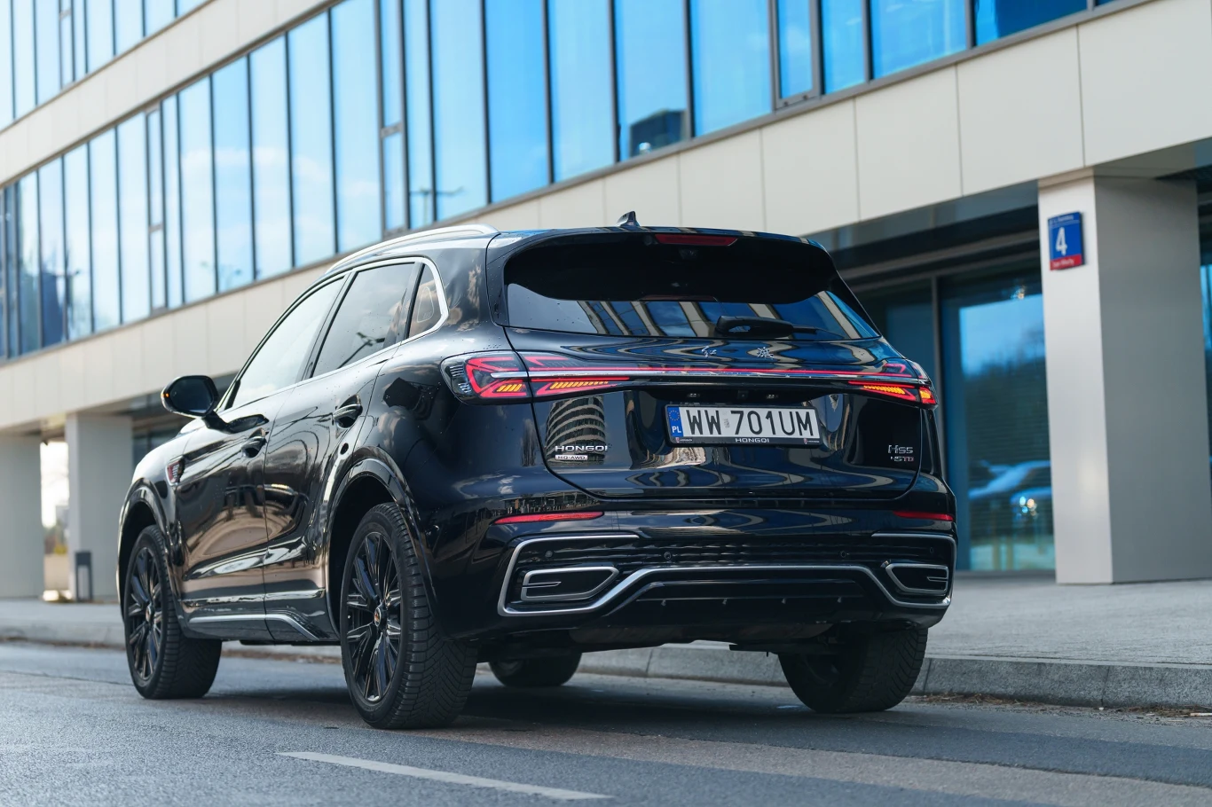Czarny SUV zaparkowany przy krawężniku obok nowoczesnego budynku o szklanej fasadzie.