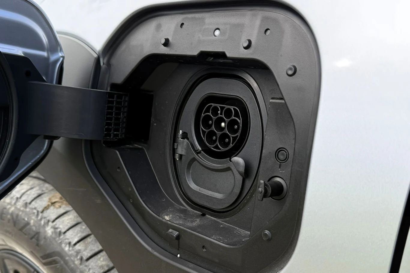 Gniazdo ładowania samochodu elektrycznego z wyraźnie widoczną wtyczką typu CCS i fragmentem koła pojazdu.