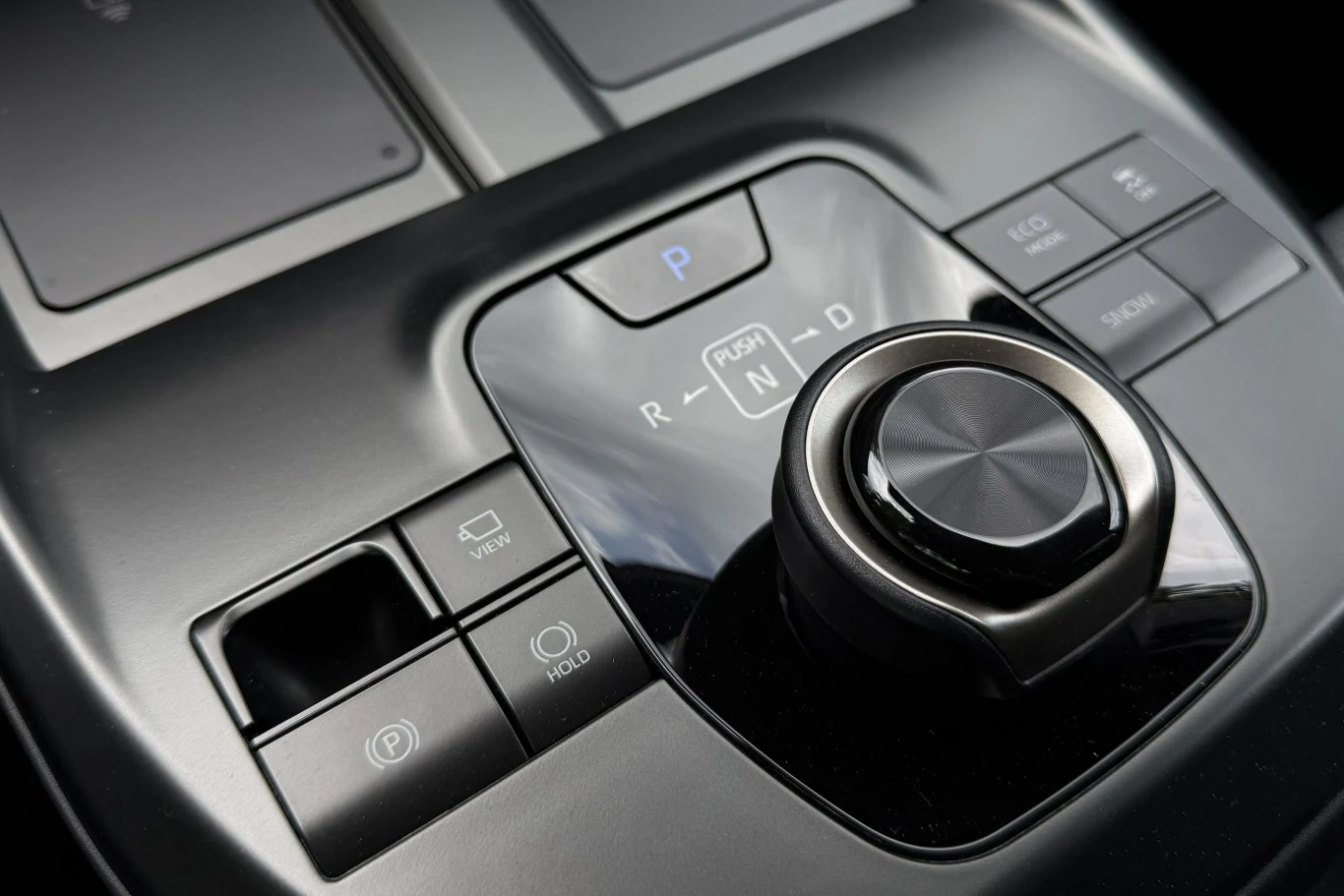 Centralny panel sterowania samochodu z nowoczesnym pokrętłem do zmiany biegów oraz przyciskami do obsługi funkcji takich jak hamulec postojowy, auto hold czy wybór trybu jazdy.