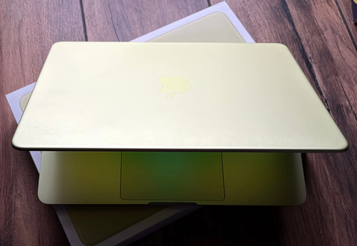 Jasnożółty laptop Apple częściowo otwarty, ustawiony na oryginalnym pudełku na drewnianej powierzchni.
