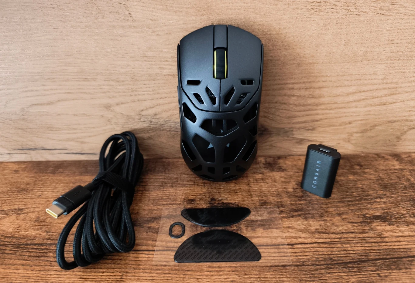 Czarna, perforowana mysz bezprzewodowa wraz z akcesoriami: odłączanym kablem USB-C, adapterem bezprzewodowym oraz dwoma wymiennymi, karbonowymi nakładkami i gumowym pierścieniem na przycisk.