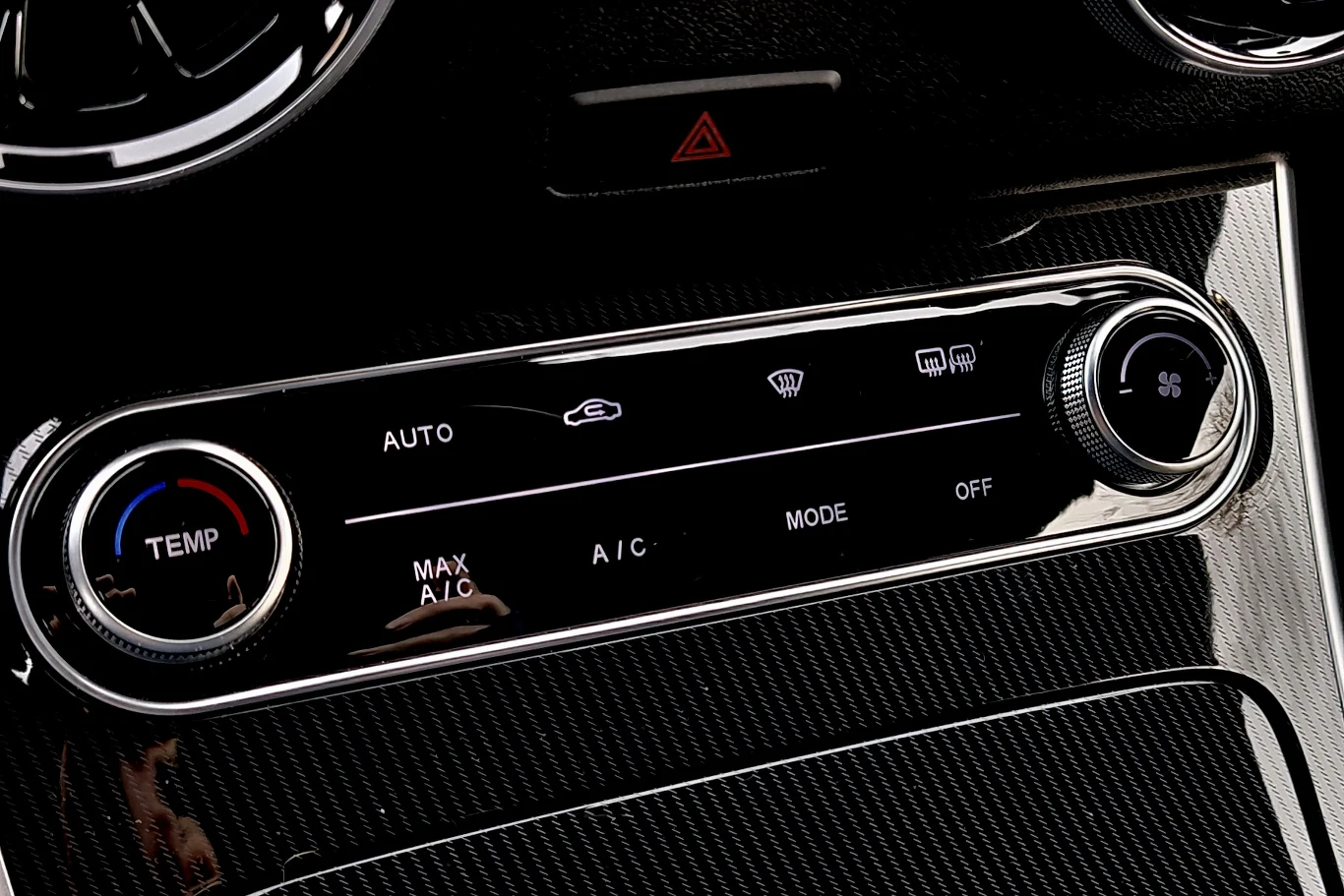 Panel sterowania klimatyzacją samochodową z elektronicznymi przyciskami do regulacji temperatury, nawiewu i trybu pracy, otoczony czarnym, połyskującym wykończeniem.