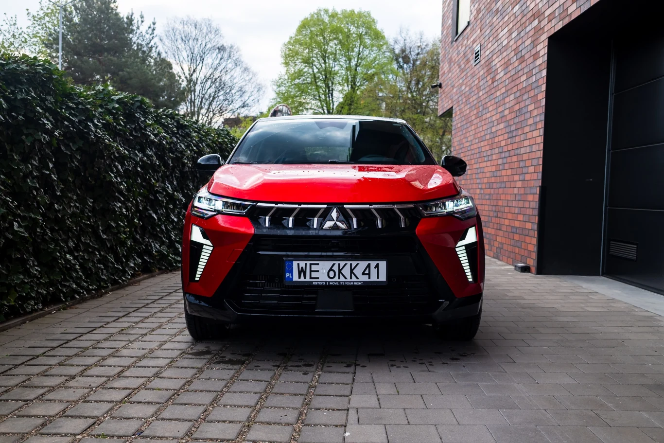 W tej kwestii nie ma już dyskusji. Mitsubishi ASX po face-liftingu wygląda bardzo zadziornie. Czerwony SUV Mitsubishi z jasnymi światłami LED i warszawską tablicą rejestracyjną, zaparkowany przodem przy ceglanej ścianie budynku.