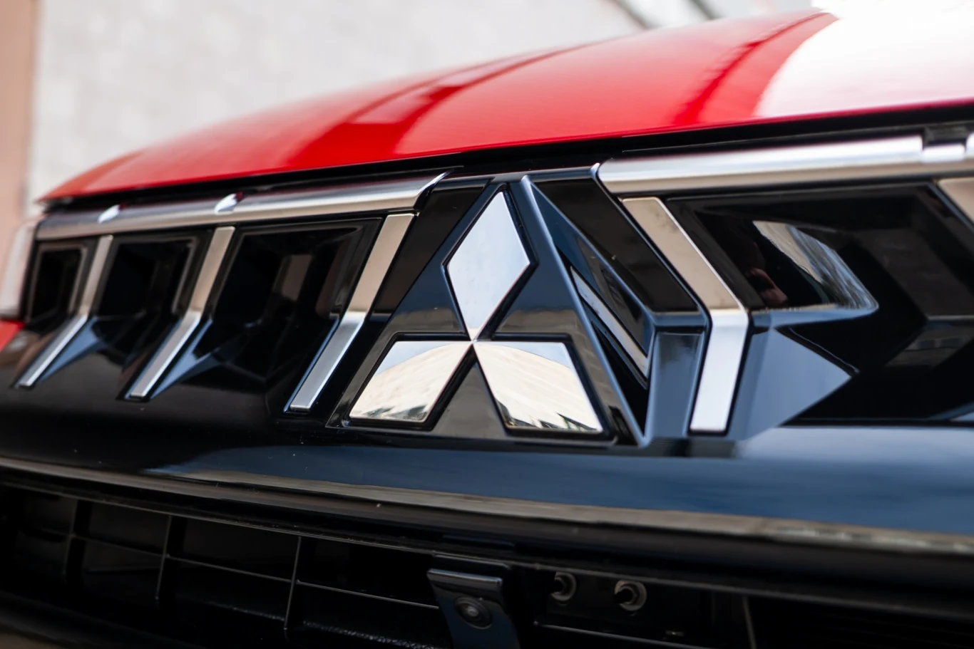 Mitsubishi ASX ma mocną konkurencję w segmencie SUV-B. Naturalnym przeciwnikiem jest oczywiście Renault Captur. Chromowany emblemat Mitsubishi umieszczony na czarnym grillu samochodu w kolorze czerwonym.