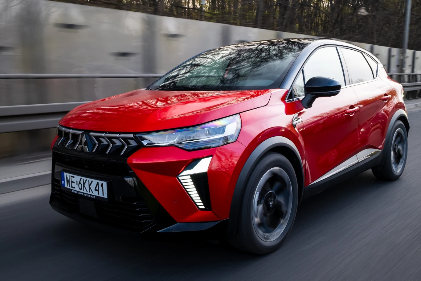 Mitsubishi ASX jest naszpikowany nowoczesnymi systemami wspomagającymi bezpieczeństwo. Pod tym względem nie odstaje od konkurencji. Czerwony nowoczesny SUV jadący po asfaltowej drodze, wyróżniający się dynamiczną linią nadwozia oraz charakterystycznym wzorem świateł LED z przodu.