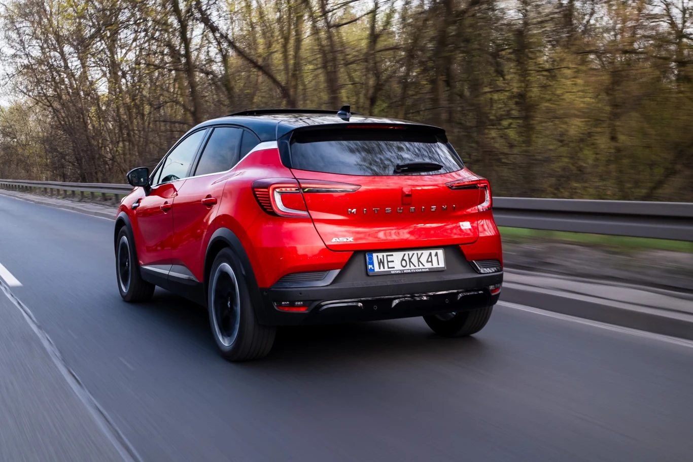 Mitsubishi ASX przejedzie w teście długodystansowym kilkanaście tysięcy kilometrów. Na koniec zajrzymy we wszystkie newralgiczne punkty tego samochodu. Czerwony samochód typu SUV marki Renault jedzie asfaltową drogą, otoczoną drzewami z widocznymi rejestracjami i charakterystycznymi czarnymi detalami nadwozia.