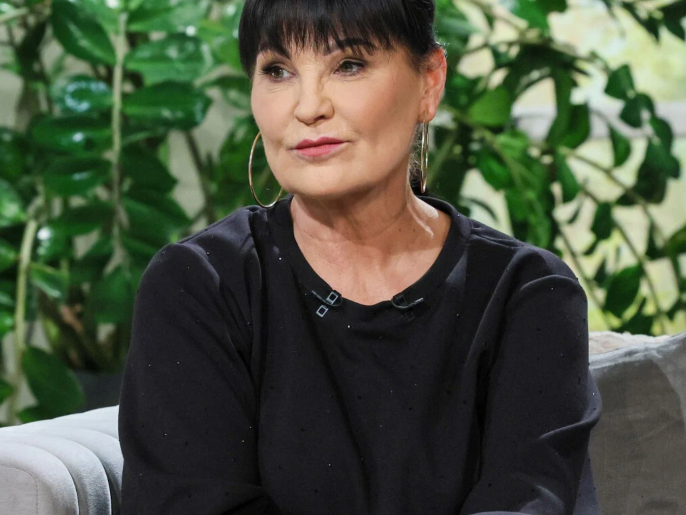 Iwona Pavlović Iwona Pavlović z krótkimi ciemnymi włosami siedzi na kanapie, w tle roślinność.