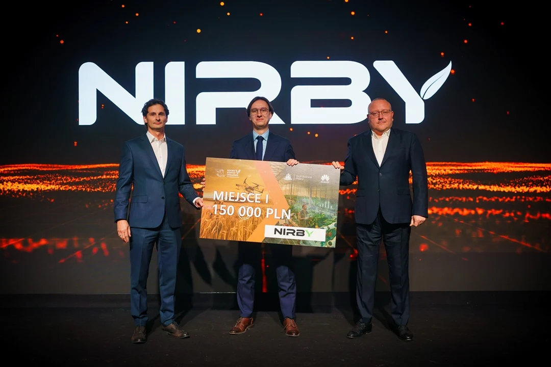 Trzech mężczyzn w garniturach trzyma dużą tablicę z napisem informującym o nagrodzie 150 000 PLN oraz logo marki NIRBY na tle dynamicznej, podświetlonej sceny.