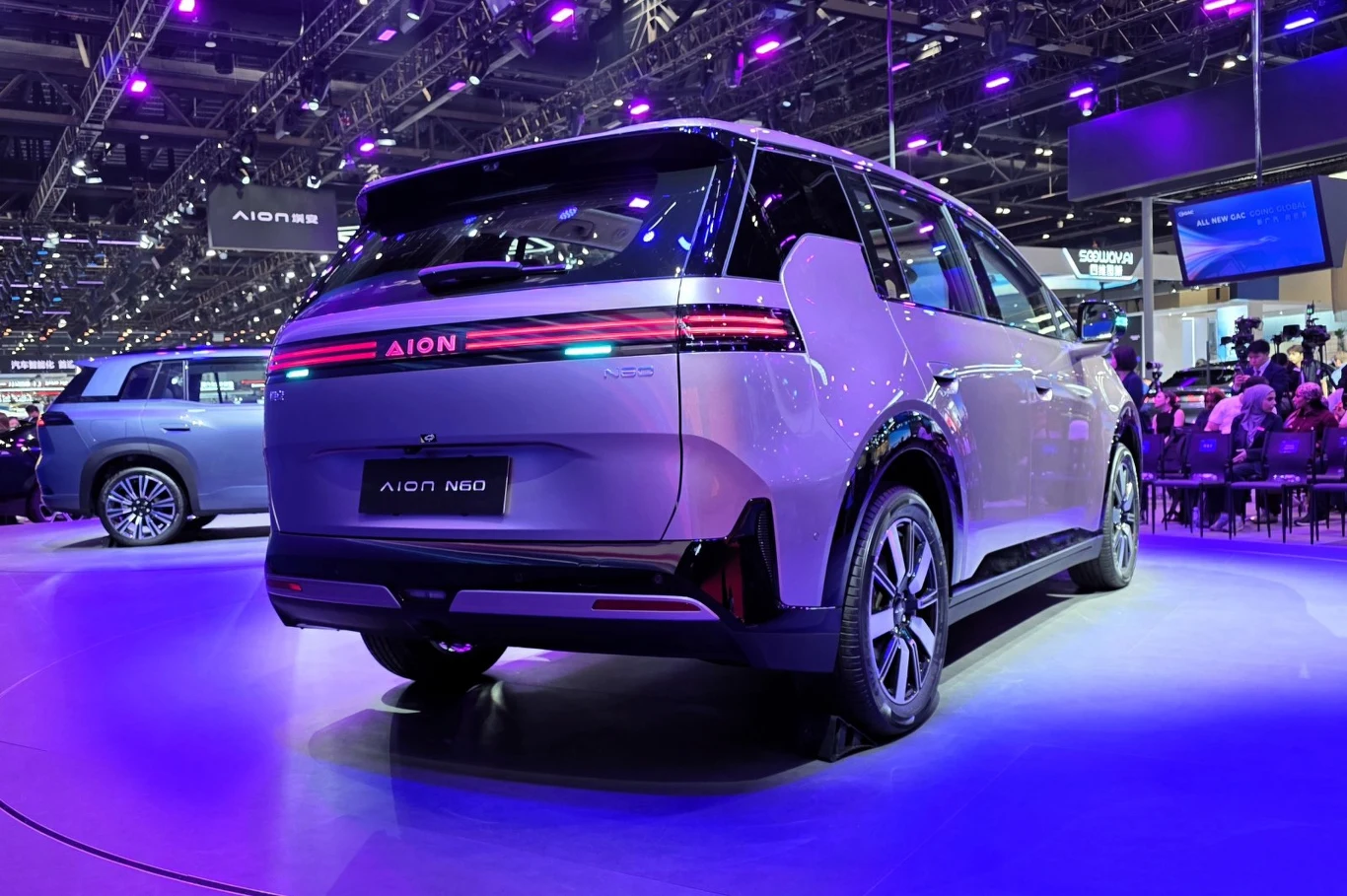 Nowoczesny samochód elektryczny Aion NX, prezentowany pod intensywnym, fioletowym oświetleniem targów motoryzacyjnych, wyróżnia się poziomą listwą świateł LED oraz charakterystycznym, futurystycznym designem nadwozia.