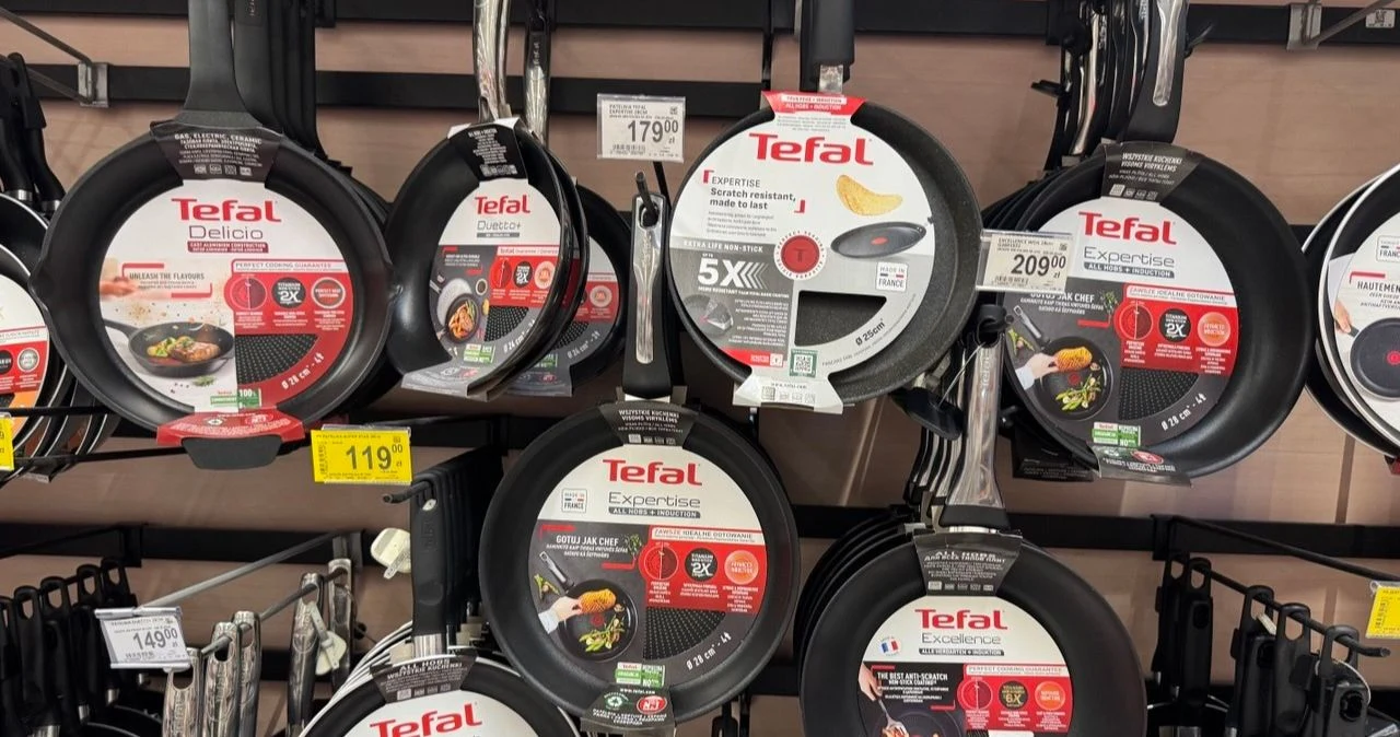 Patelnie Tefal w Auchan mocno potaniały. Niektóre modele są tańsze nawet o 42% Patelnie Tefal w różnych rozmiarach z etykietami i cenami zawieszone na sklepowych hakach w Auchan