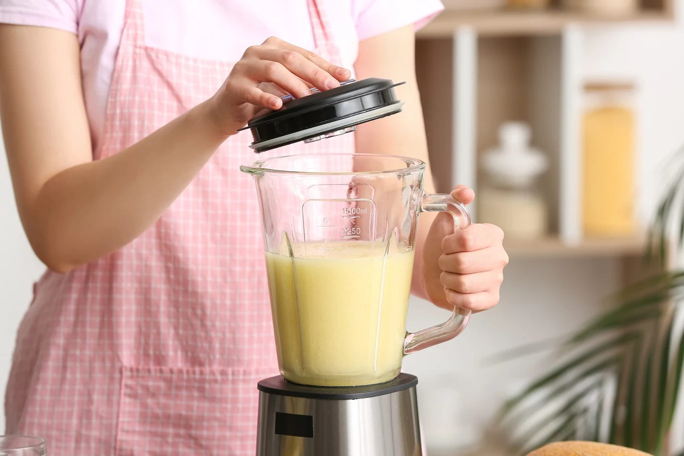 Zdrowy koktajl z mango. Smakowita propozycja na kolację. Koktajl z mango w blenderze, osoba w różowym fartuchu nakłada pokrywkę na blender.