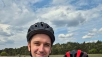 Dwie osoby w sportowych koszulkach i kaskach rowerowych trzymają medale z napisem JYSK, uśmiechając się do aparatu podczas wydarzenia na świeżym powietrzu.