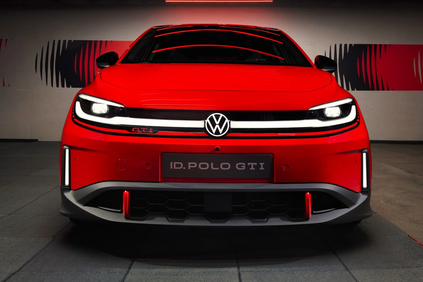 Czołowy widok czerwonego Volkswagena ID. Polo GTI z charakterystycznym znakiem VW na środku maski, dynamicznymi reflektorami LED i sportowym, agresywnym zderzakiem.