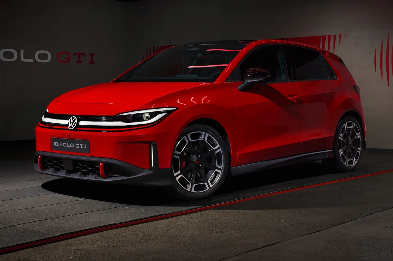 Czerwony Volkswagen Polo GTI na ciemnym tle, z charakterystycznymi sportowymi felgami i agresywnie stylizowanym przednim zderzakiem podkreślającym dynamiczny wygląd auta.