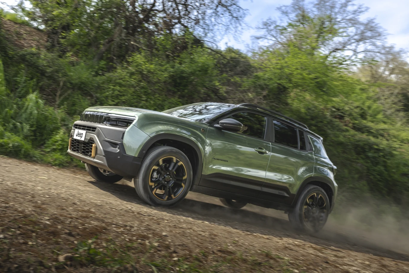 Zielony SUV marki Jeep porusza się po nieutwardzonej, leśnej drodze, otoczony gęstą zielenią i drzewami.