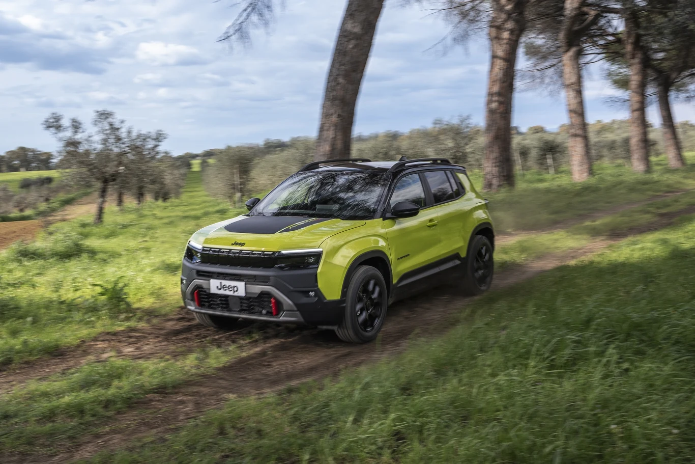 Żółto-czarny samochód Jeep jedzie polną drogą otoczoną drzewami i zieloną trawą.