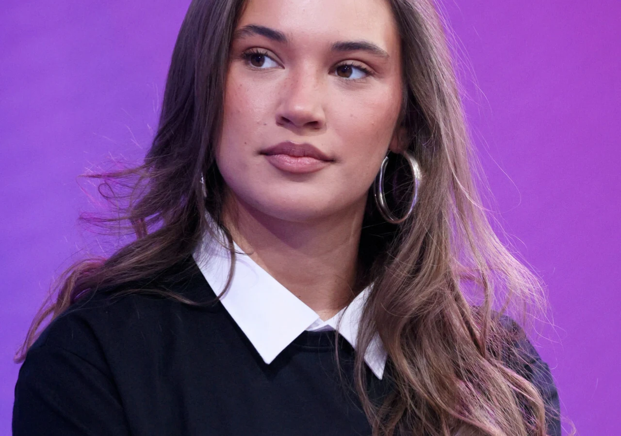 Alicja Szemplińska Alicja Szemplińska z długimi brązowymi włosami w czarnym swetrze z białym kołnierzykiem na fioletowym tle.