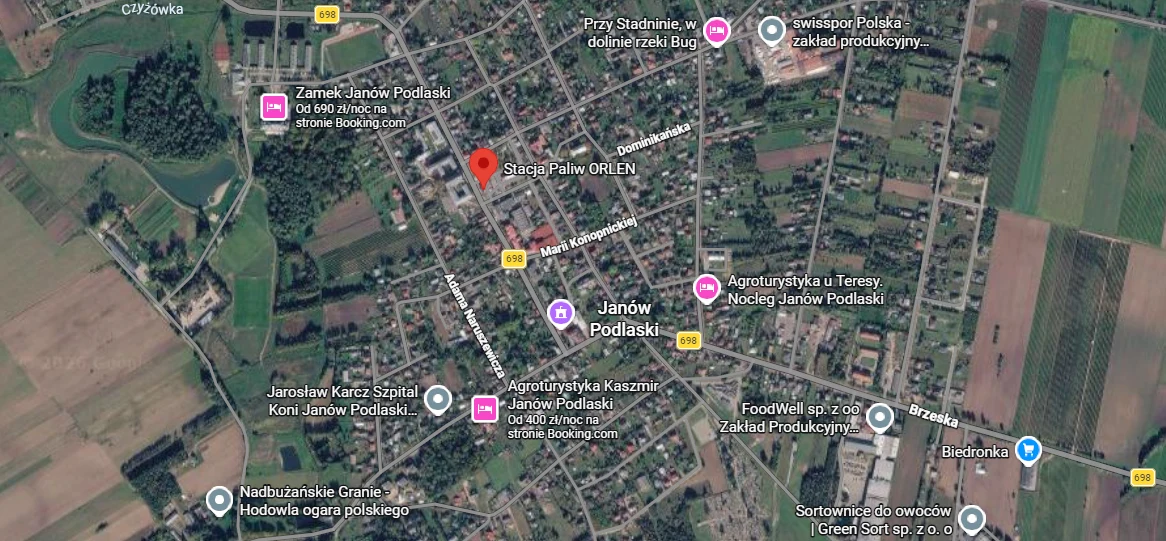 Centrum Janowa Podlaskiego z oznaczonymi ważnymi punktami, takimi jak stacja paliw, Biedronka, zamek i stadnina, otoczone polami uprawnymi oraz zabudową mieszkalną.