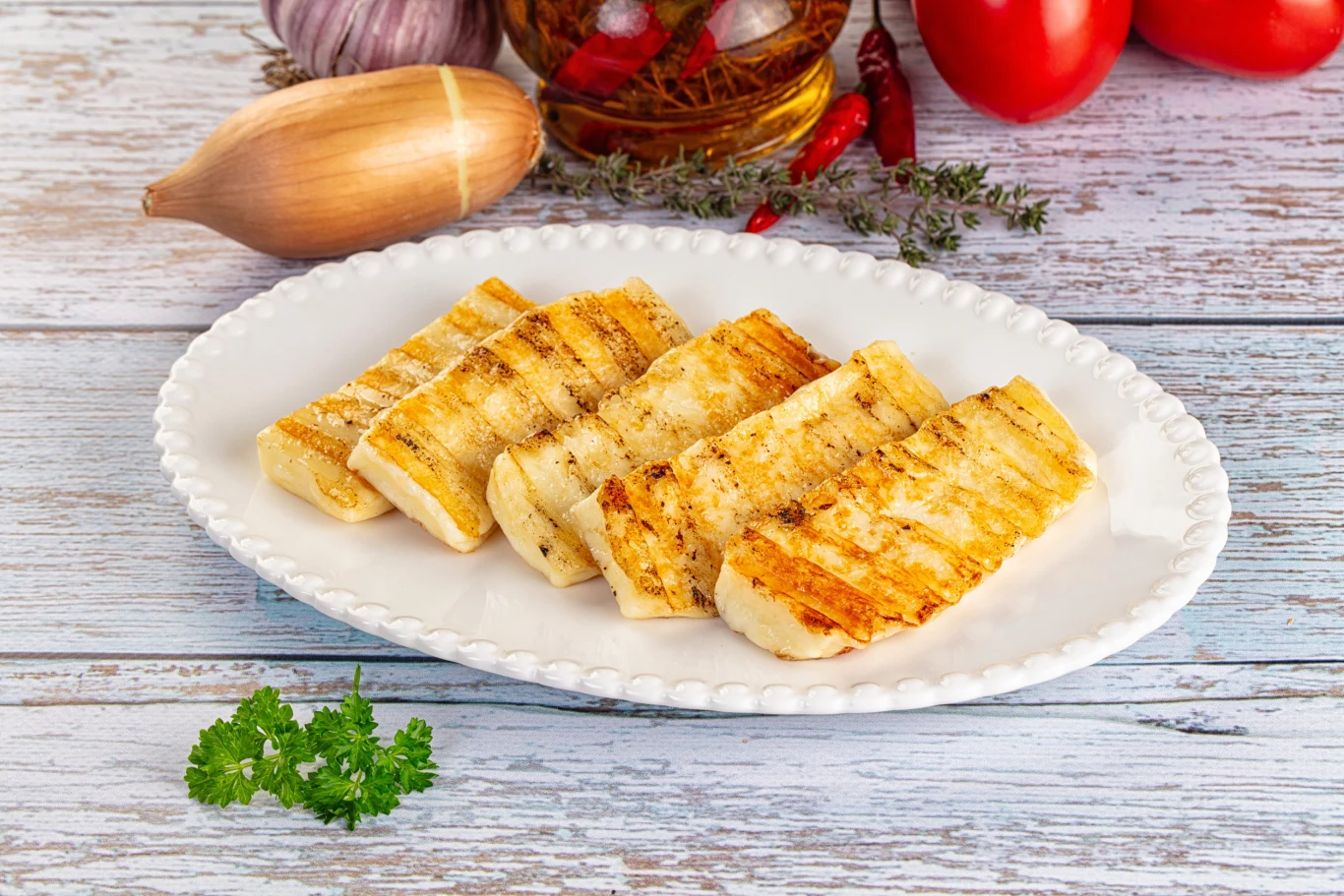 Ser halloumi w wersji grillowanej smakuje doskonale Plastry grillowanego sera halloumi na białym talerzu, udekorowane świeżą natką pietruszki.