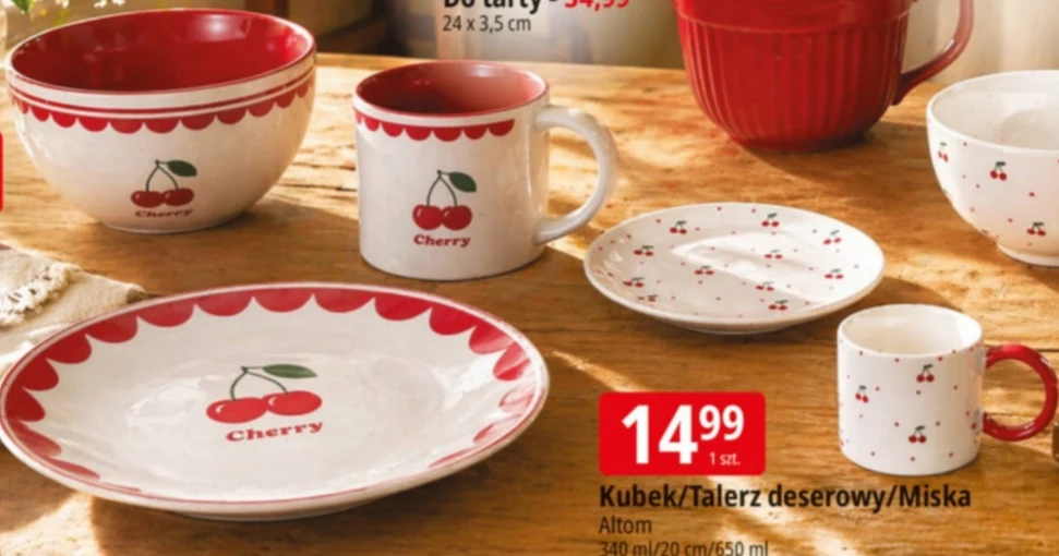 Zestaw naczyń ceramicznych ozdobionych motywem czerwonych wisienek z czerwonymi rantami, obejmujący kubki, miski i talerze ustawione na drewnianym stole obok oznaczenia promocyjnej ceny.