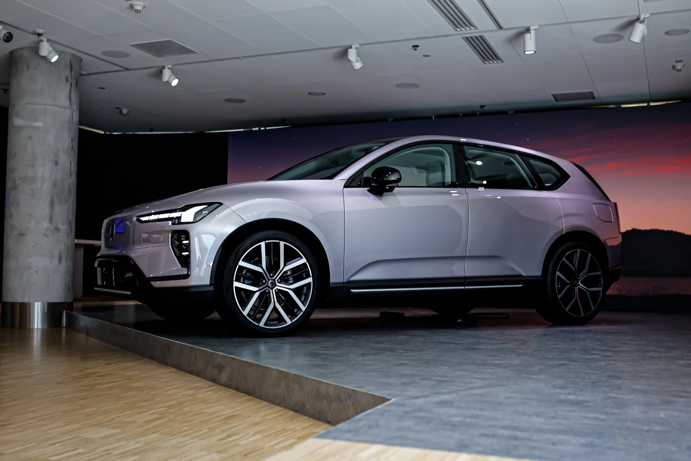 Srebrny nowoczesny SUV o dynamicznej sylwetce, dużych alufelgach i charakterystycznym przodzie, ustawiony na podwyższonej platformie w jasnym, przestronnym wnętrzu ekspozycyjnym.
