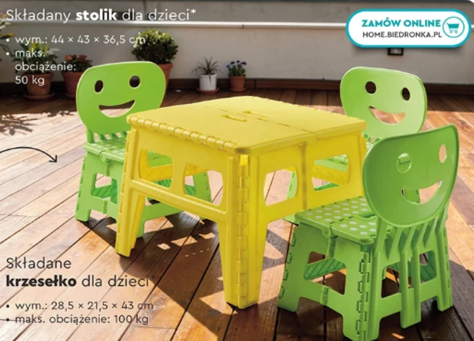 Kolorowy, plastikowy stolik oraz cztery składane krzesełka dla dzieci z wyciętymi uśmiechniętymi buźkami, ustawione na tarasie z drewnianą podłogą.