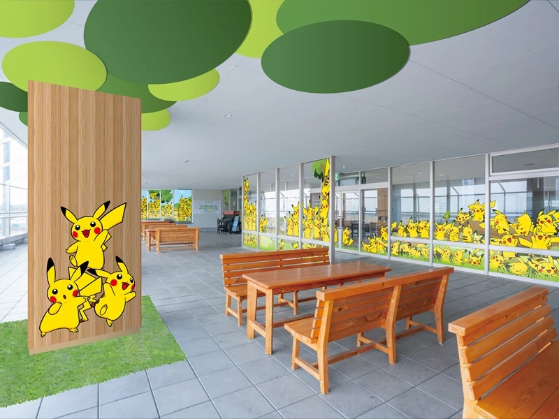 Drewniane ławki i stoły ustawione w przestronnej, jasnej sali ozdobionej licznymi rysunkami Pikachu na szklanych ściankach działowych oraz na słupie, zielone dekoracje sufitowe przypominające liście.