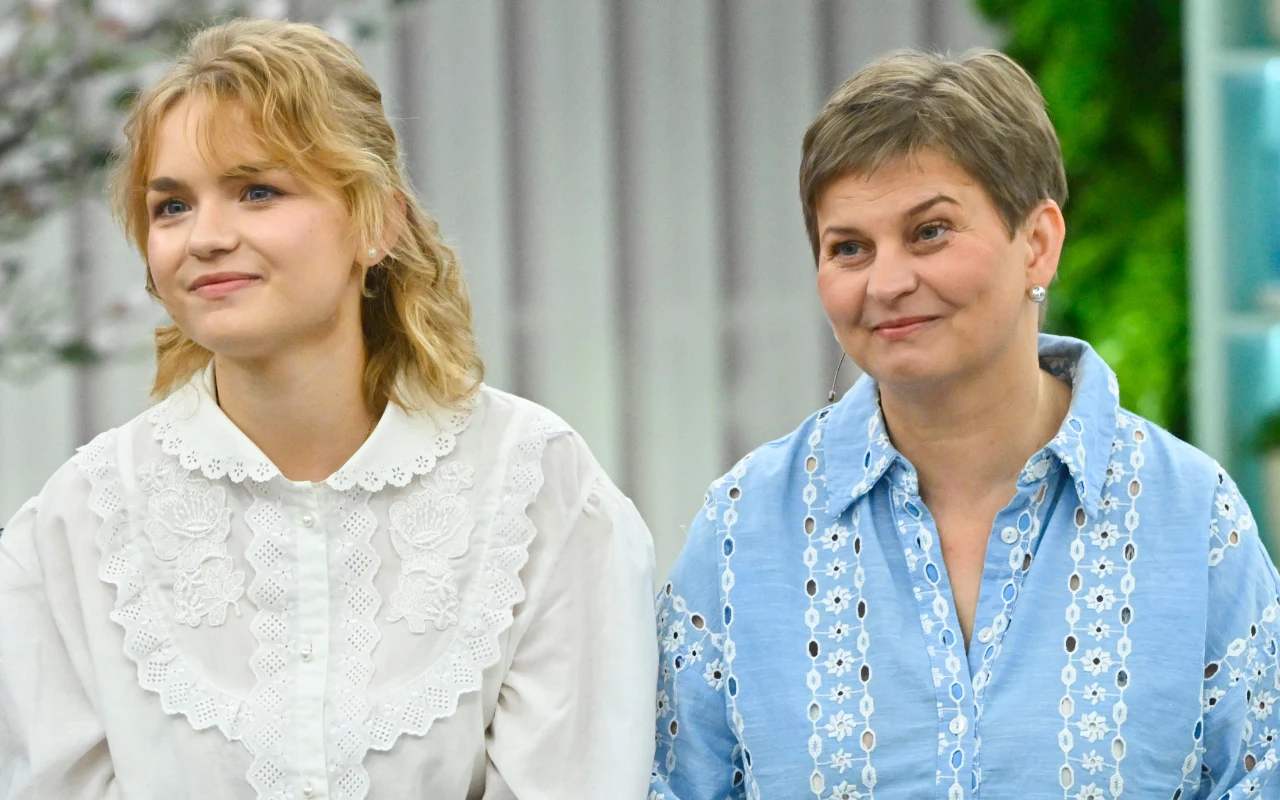 Mama Marceliny, Grażyna, nie kryła dumy z sukcesu córki Dwie uśmiechnięte kobiety siedzą obok siebie, jedna w białej bluzce z dużym kołnierzem, druga w niebieskiej koszuli z białym wzorem ażurowym.