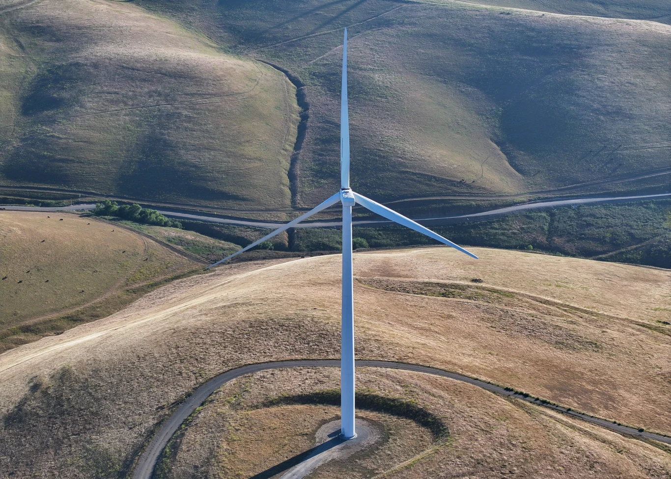 Na razie nie ma potwierdzenia, że infradźwięki emitowane przez turbiny wiatrowe wpływają na zdrowie Pojedyncza turbina wiatrowa ustawiona pośrodku rozległego, pagórkowatego krajobrazu pokrytego suchą trawą, otoczona krętą asfaltową drogą.