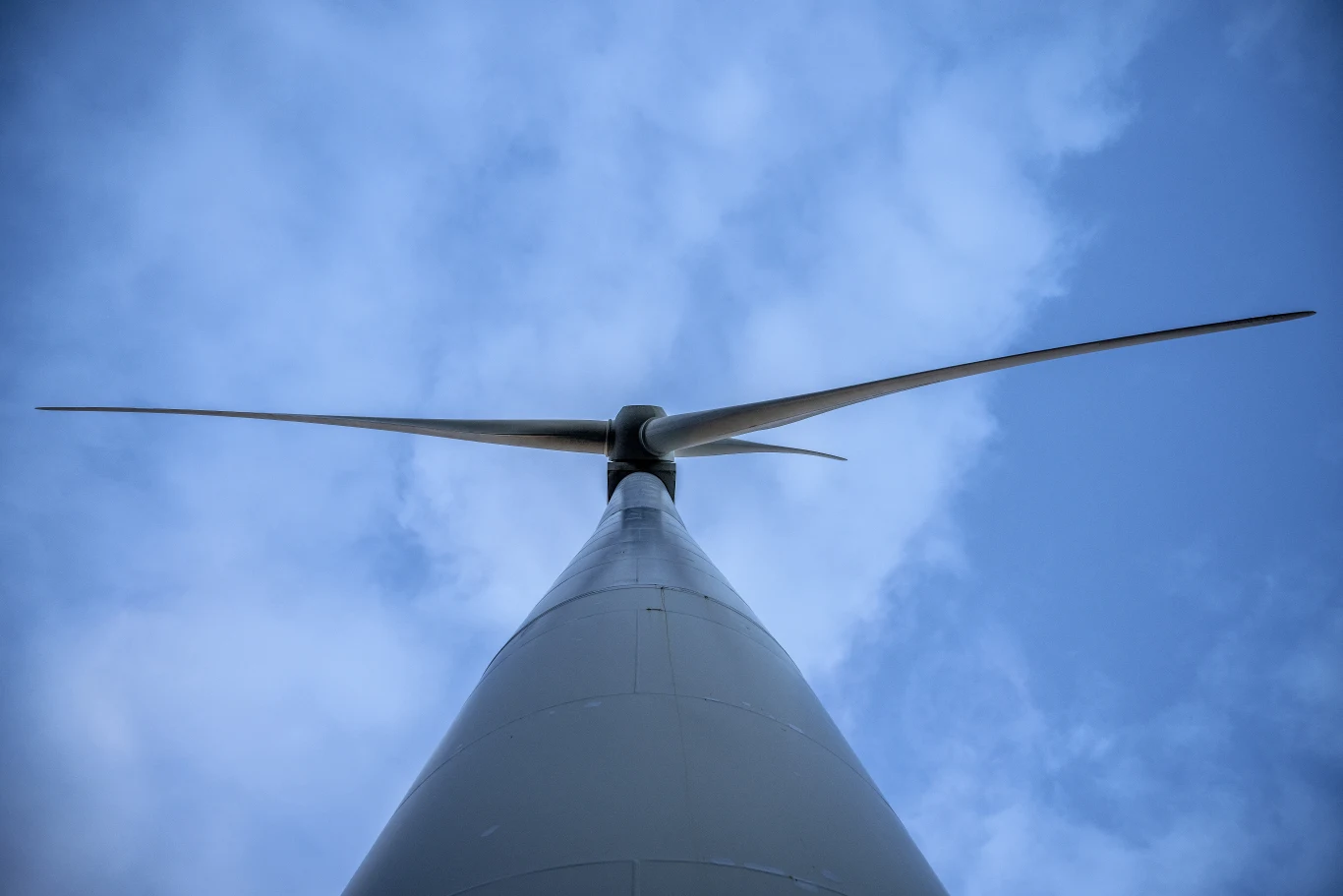 Długotrwały wpływ wiatraków na zdrowie nie jest dobrze zbadany Nowoczesna turbina wiatrowa z łopatami skierowanymi ku niebu na tle błękitnego, lekko zachmurzonego nieba.