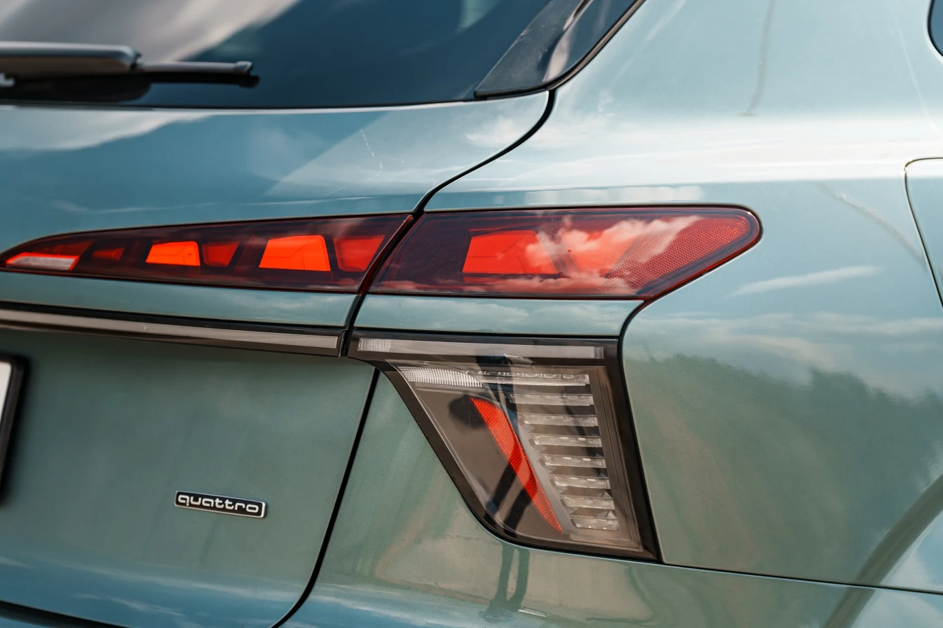 Tylna lampa LED samochodu Audi z napisem quattro na błotniku, odbijająca chmury w lakierze nadwozia.