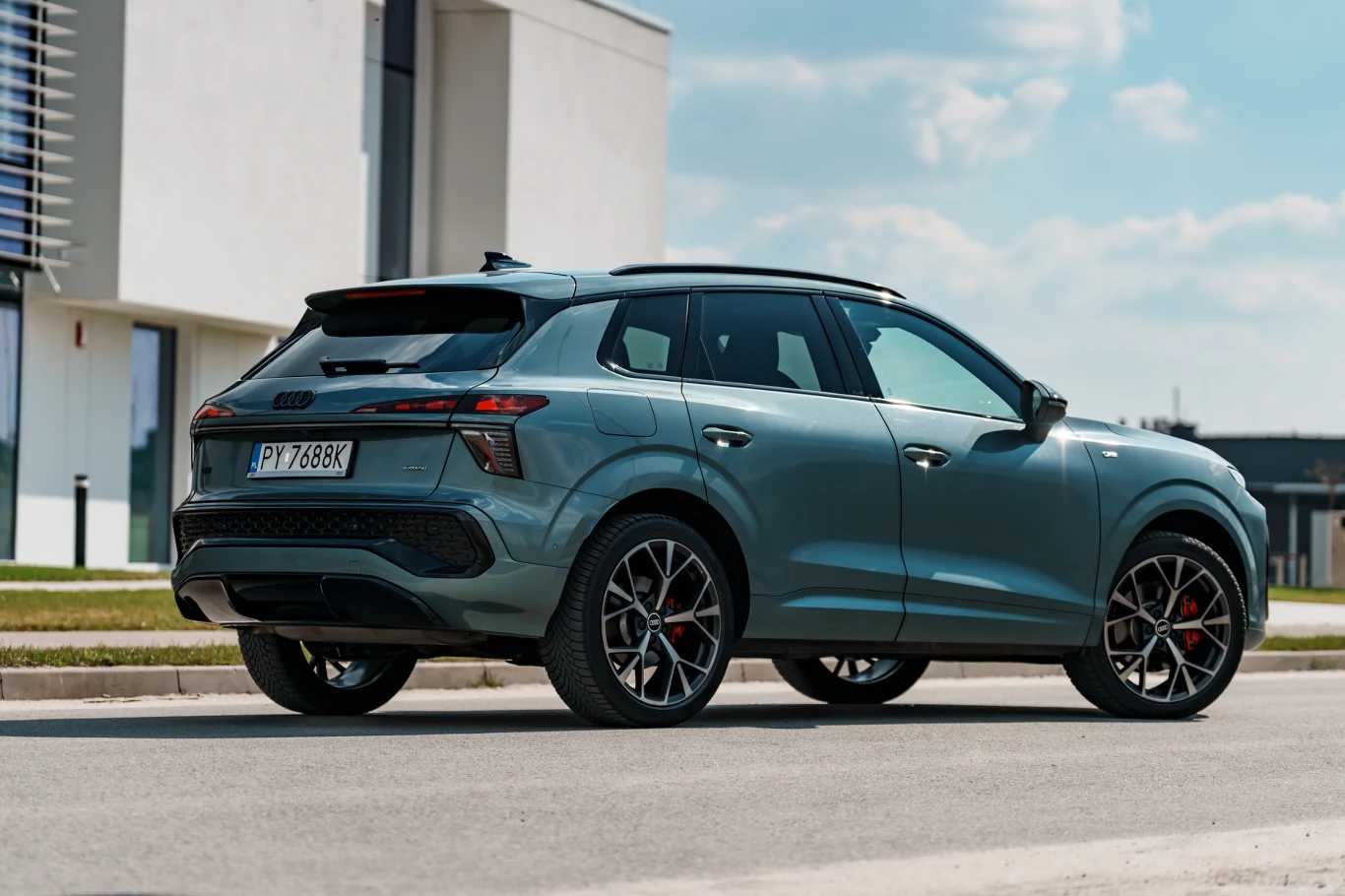 Nowoczesny, zielony SUV Audi Q6 e-tron stoi na ulicy, wyeksponowane charakterystyczne tylne światła LED oraz stylowe, ciemne alufelgi z czerwonymi zaciskami hamulców.
