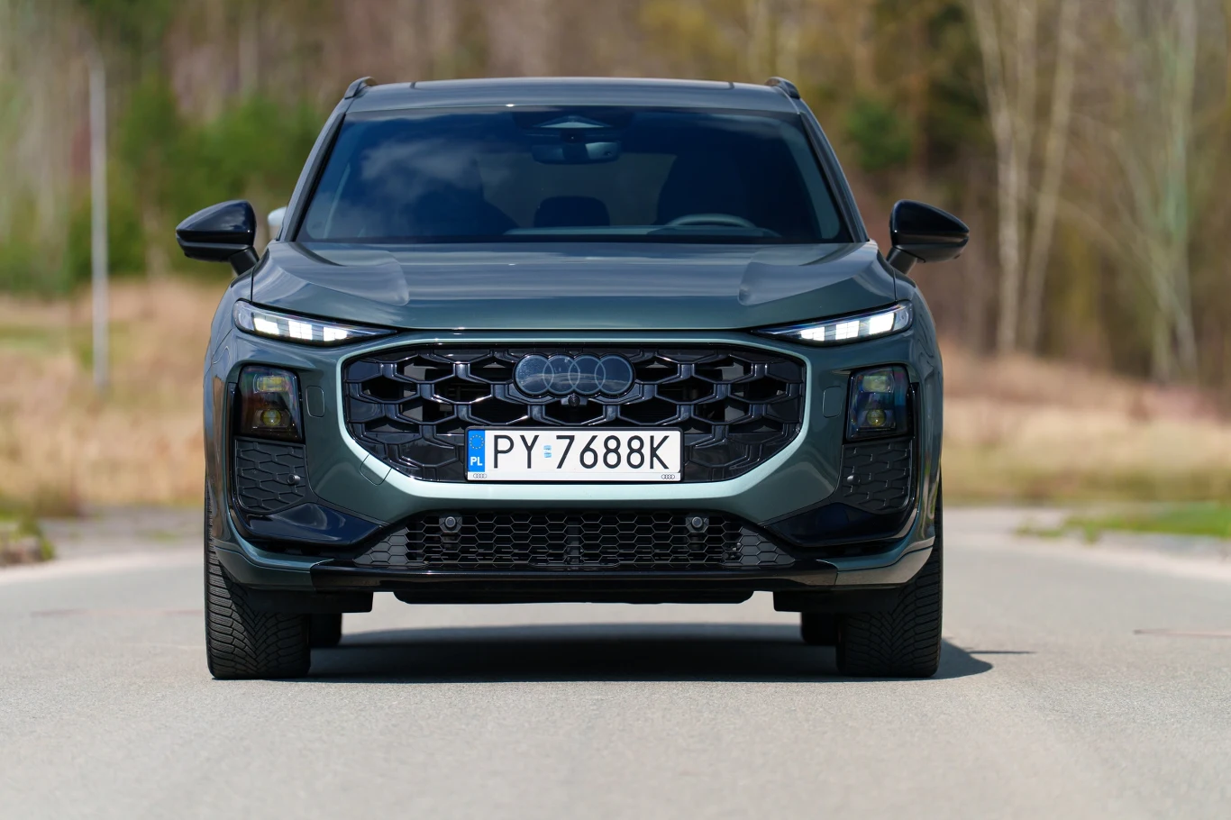 ciemnoszary SUV marki Audi z nowoczesnym grillem i charakterystycznymi, wąskimi reflektorami LED, stojący frontalnie na pustej drodze