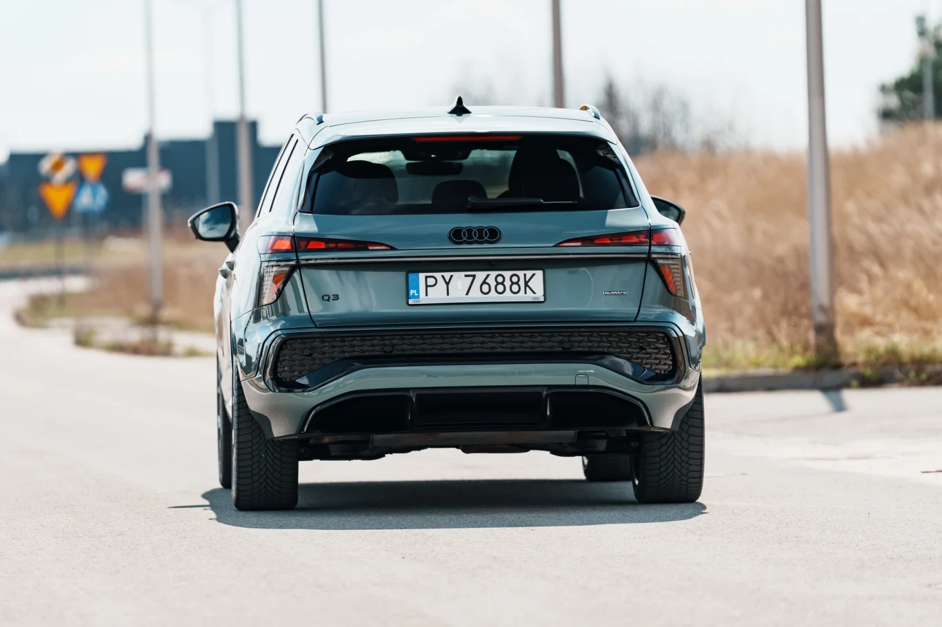 Srebrne Audi Q8 stojące na pustej, asfaltowej drodze, widoczne od tyłu, z wyraźnie widoczną tablicą rejestracyjną i charakterystycznymi, nowoczesnymi światłami LED.