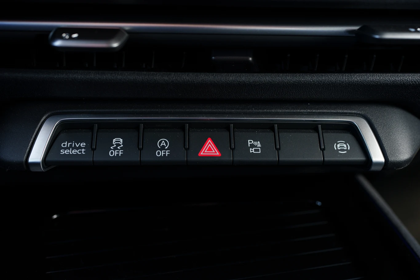 Panel przycisków w samochodzie z funkcjami takimi jak drive select, wyłączanie kontroli trakcji, system start-stop, światła awaryjne, asystent parkowania oraz elektroniczny hamulec postojowy.
