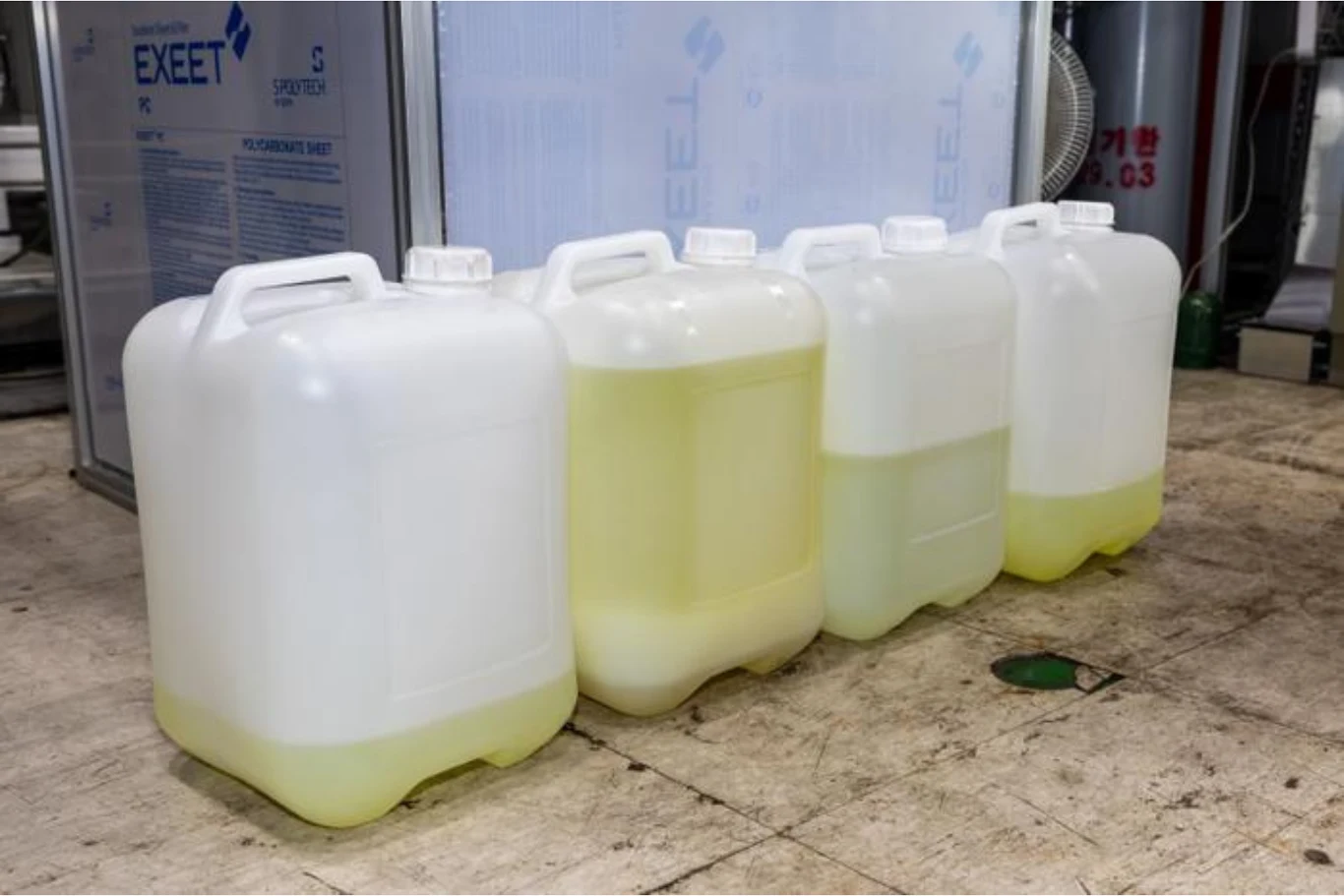 Cztery plastikowe kanistry ustawione w rzędzie, dwa z nich częściowo wypełnione żółtawą cieczą.