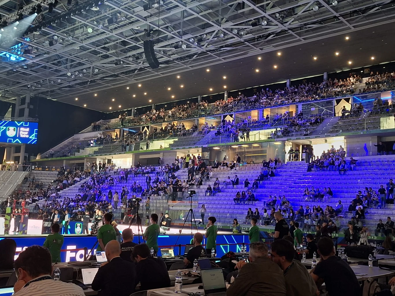 Trybuny Inalpi Areny tuż przed sobotnimi półfinałami Ligi Mistrzów siatkarzy Drużyna ubrana w zielone stroje sportowe stoi w rzędzie na tle trybun areny sportowej, wypełnionych częściowo kibicami oraz stanowiskami dla dziennikarzy z komputerami na pierwszym planie.